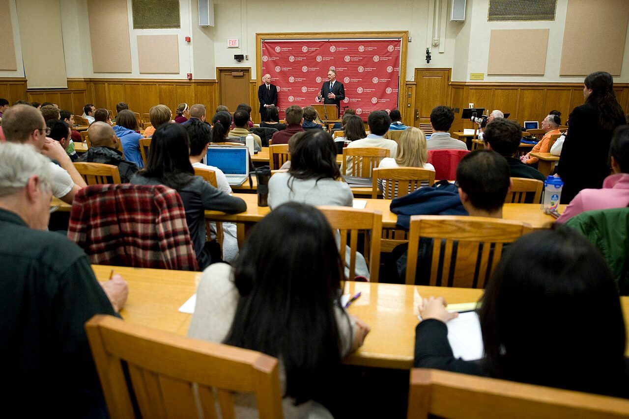 A U.S. government speaker addresses roughly 100 law students seated in a law-school auditorium at Cornell Law School.
