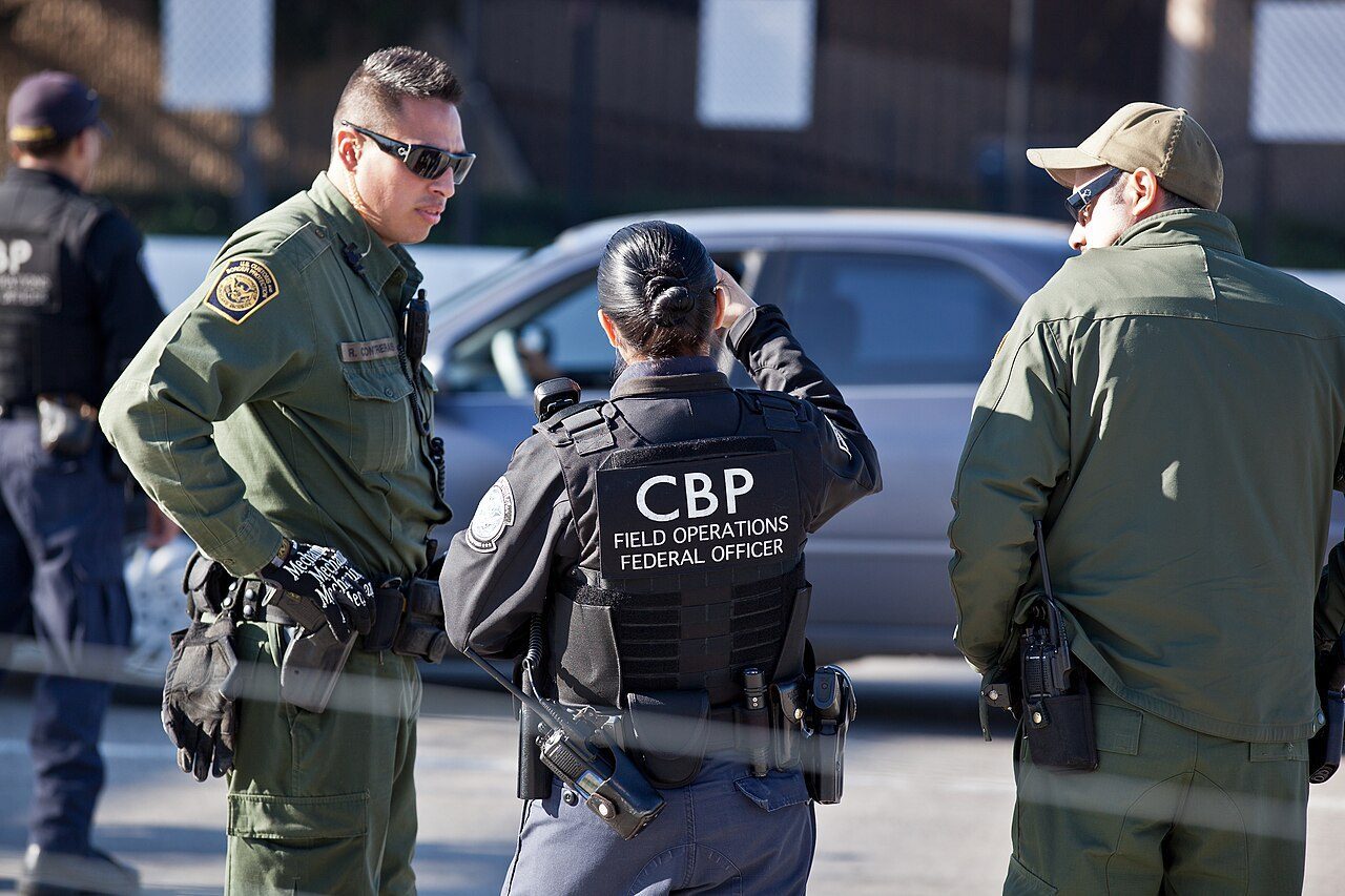 U.S. Customs and Border Protection officers, including a Field Operations federal officer, standing at the San Ysidro port of entry.