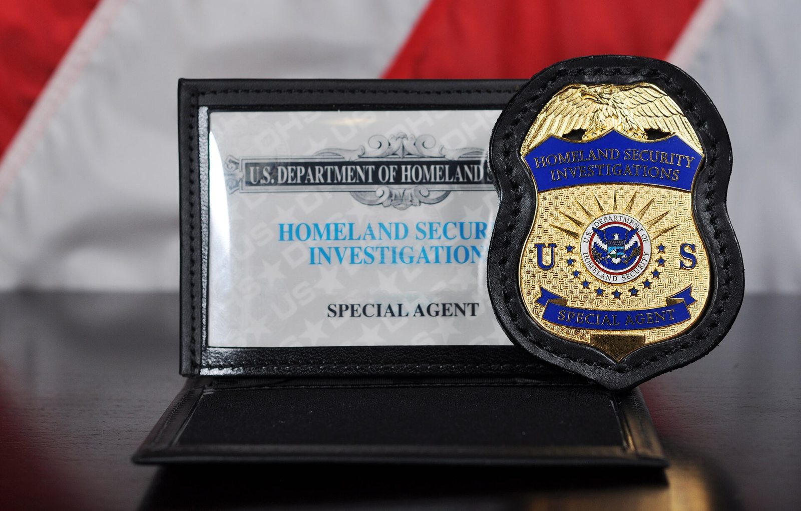 A Homeland Security Investigations special agent badge and credential case set in front of an American flag.