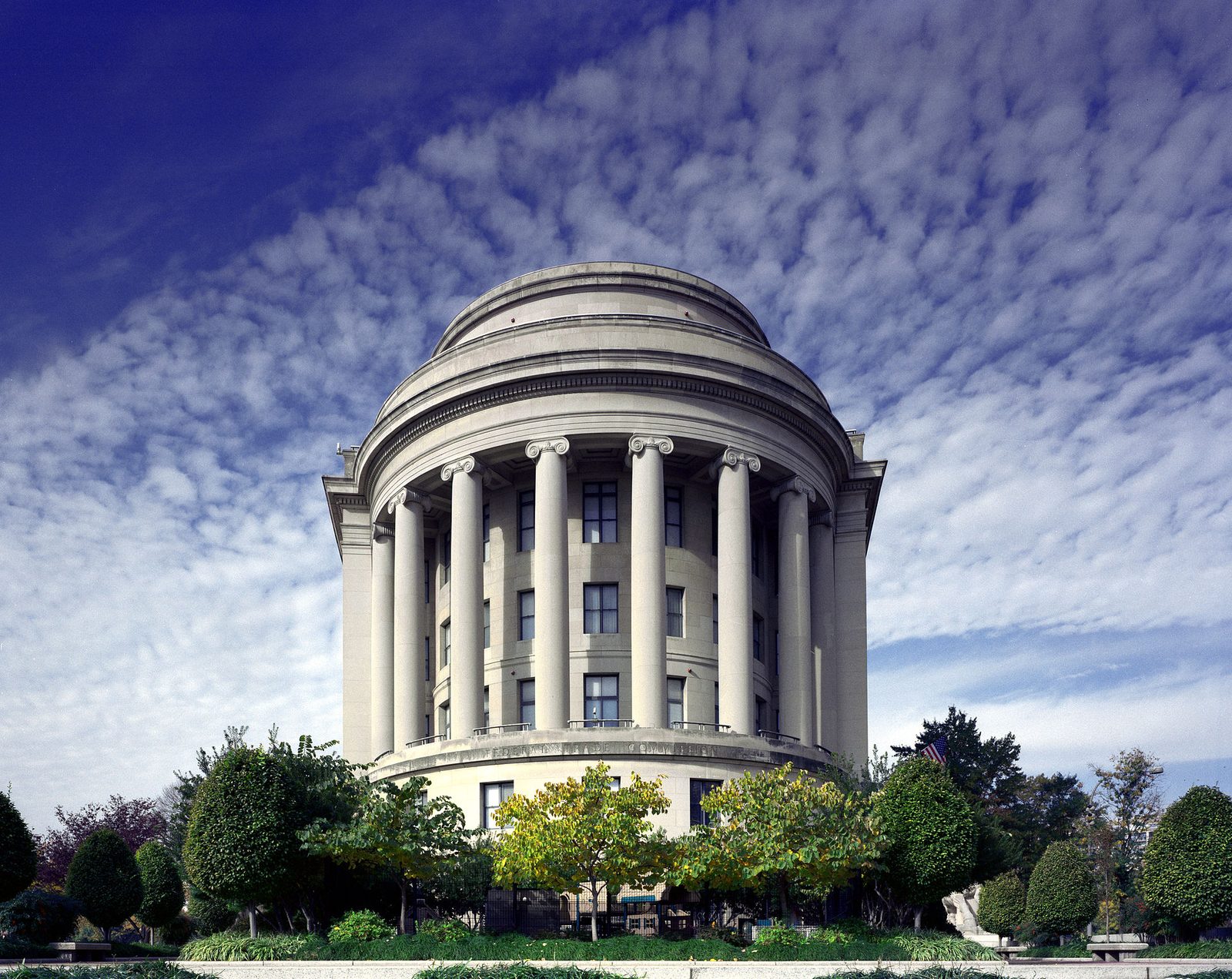 The columned rotunda of the Federal Trade Commission Building (Apex Building) in Washington, D.C., under a cloud-streaked sky.
