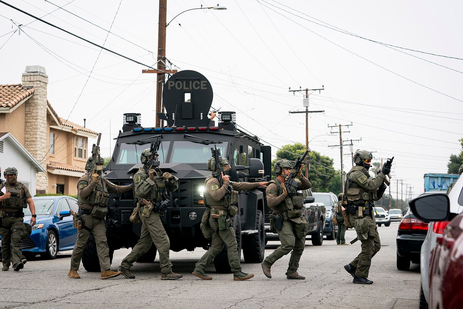 Armed ICE tactical officers advance alongside an armored vehicle on a residential street during an enforcement operation in Los Angeles, June 2025.