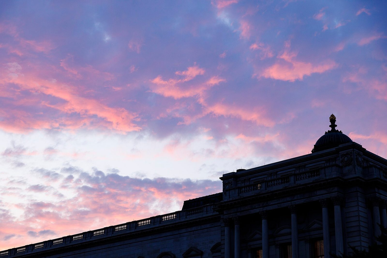 The Library of Congress Thomas Jefferson Building dome and colonnade silhouetted against a pink-and-purple sunset sky.