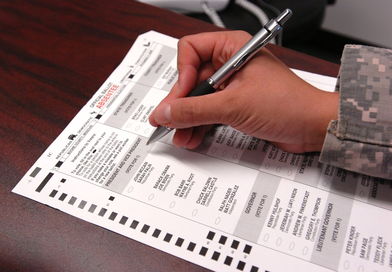 A hand holding a pen fills out a paper absentee ballot for the 2008 U.S. general election.