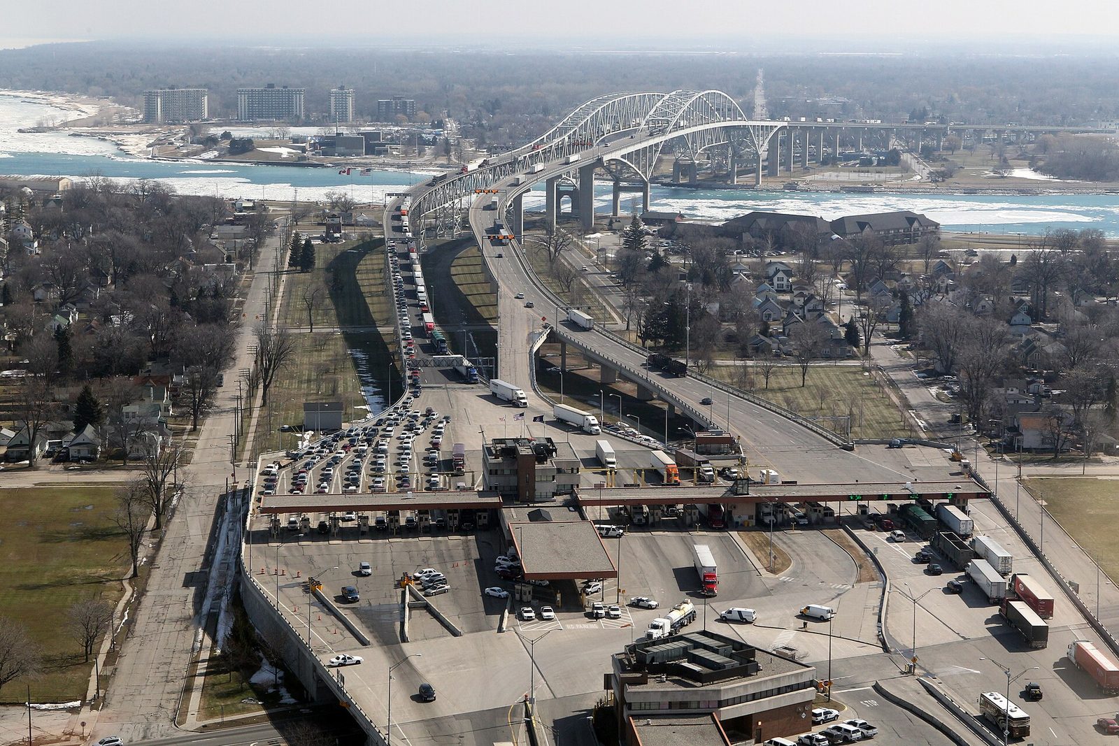 Aerial view of the Blue Water Bridge between Port Huron, Michigan, and Point Edward, Ontario, with trucks and cars queued at the U.S. port of entry.