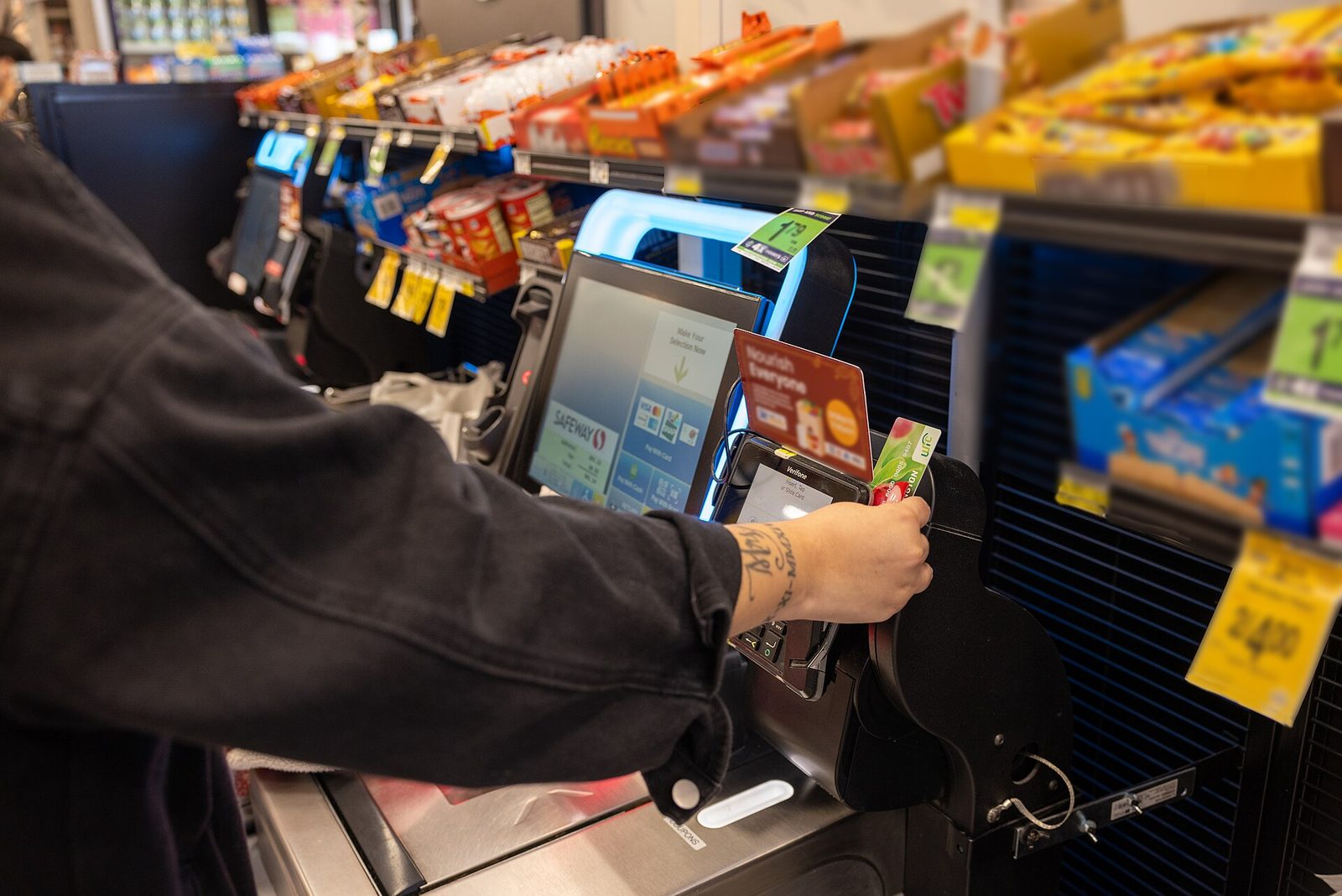 A shopper swipes an EBT benefits card at a grocery-store self-checkout terminal.